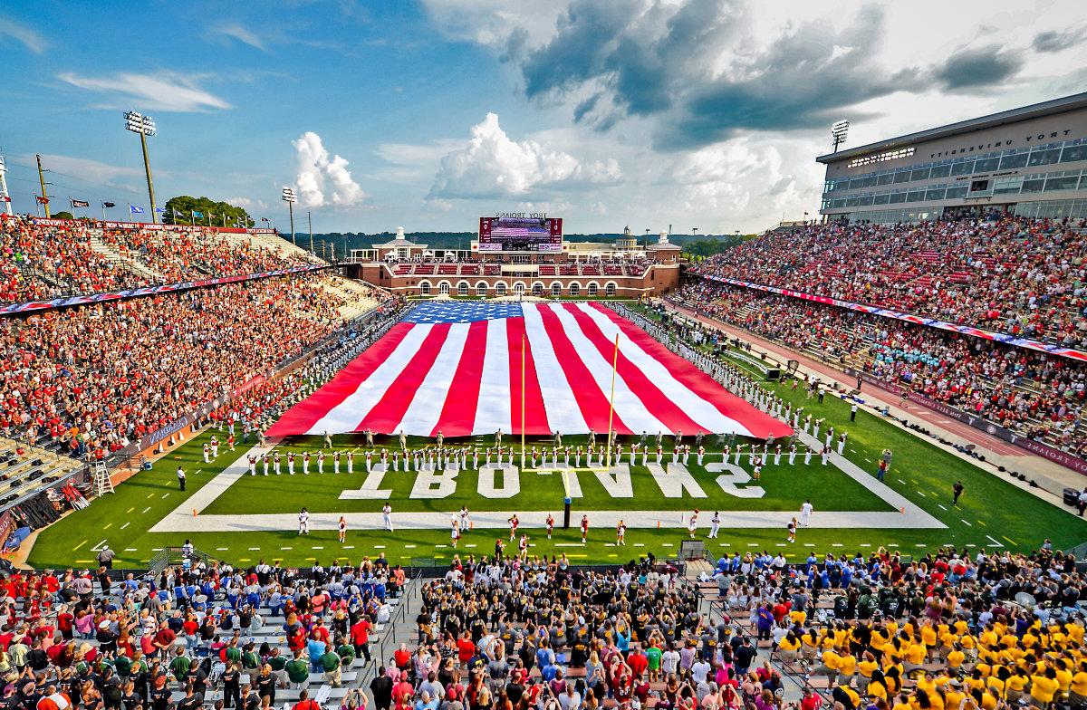 Large American flag spread across football field by marching band